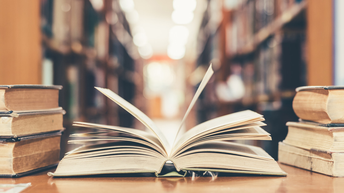 Otwoarta książka na stole a w tle biblioteczne regały